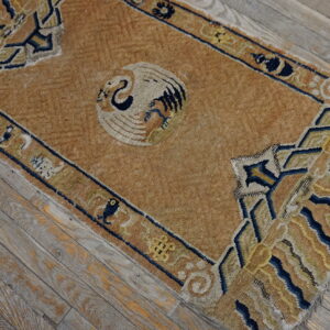 Aged tan rug with a central stylized bird and blue geometric border on weathered wooden flooring.