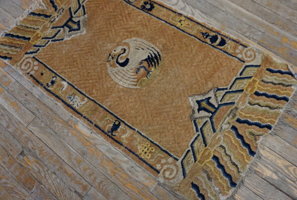 Aged tan rug with a central stylized bird and blue geometric border on weathered wooden flooring.