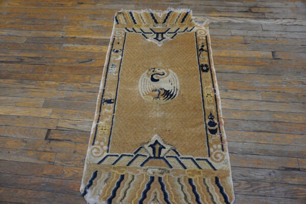 Tan runner rug featuring a central white bird motif and navy blue geometric borders on distressed wood planks.
