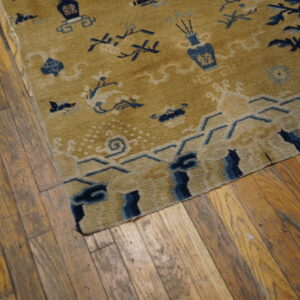 A low-pile gold rug with blue decorative motifs rests on worn hardwood planks.