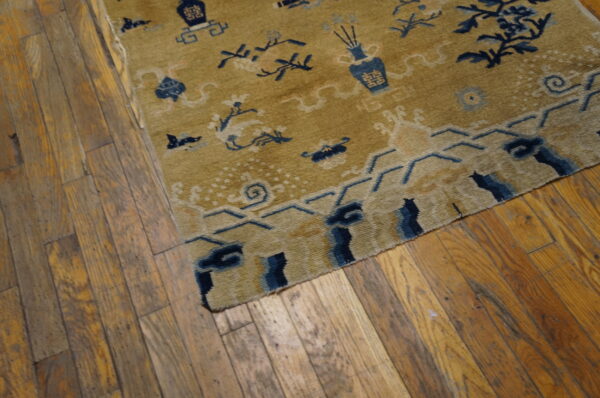 A low-pile gold rug with blue decorative motifs rests on worn hardwood planks.