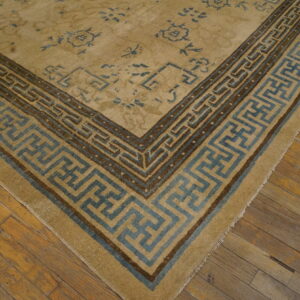 A tan rug with geometric blue and brown borders rests on rustic, warm-toned wood planks.