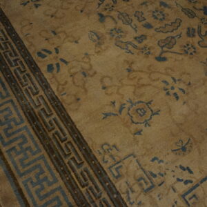 Tan rug with sparse blue floral patterns and a wide fretwork border on dark wood flooring.