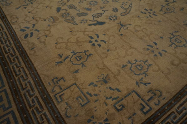 Muted beige rug with antique blue floral patterns and a dark brown geometric key border.