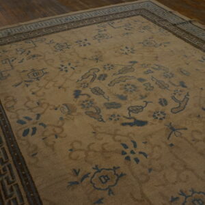 Low-pile tan rug featuring blue and brown floral patterns and key borders on dark hardwood.