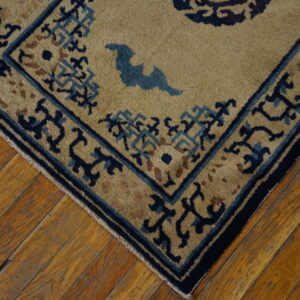 Corner of a tan rug with intricate blue and navy border designs on distressed hardwood planks.