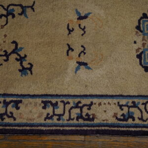 Muted gold rug featuring dark blue, light blue, and brown motifs, bordered on rustic wood flooring.