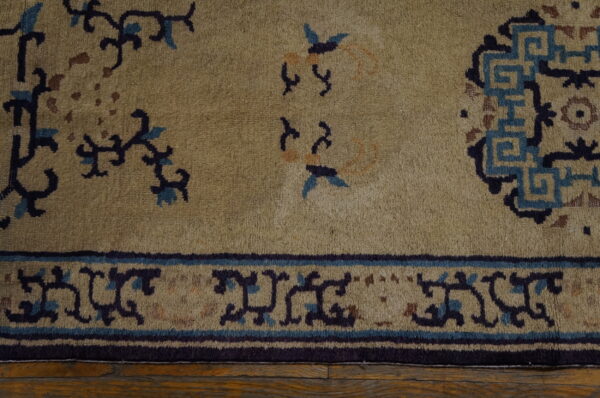 Muted gold rug featuring dark blue, light blue, and brown motifs, bordered on rustic wood flooring.