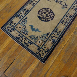 Tan rug with blue geometric borders and stylized patterns rests on distressed golden wood flooring.