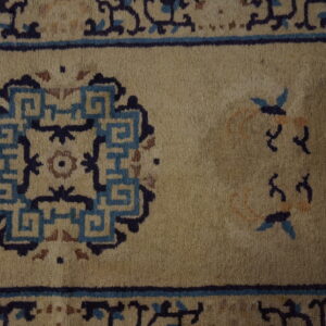 Muted beige rug surface detail showing dark blue geometric medallions and stylized floral accents.