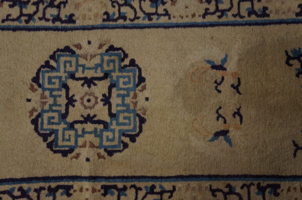 Muted beige rug surface detail showing dark blue geometric medallions and stylized floral accents.