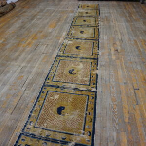 Worn gold and blue runner with repeating geometric panels and central motifs on an old wood floor.