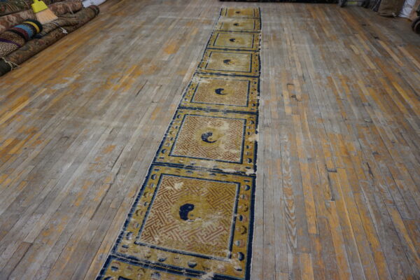 Worn gold and blue runner with repeating geometric panels and central motifs on an old wood floor.
