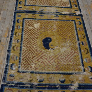 Worn gold and indigo low-pile runner rug with a geometric key pattern on distressed wood planks.