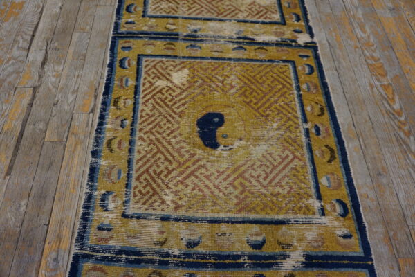 Worn gold and indigo low-pile runner rug with a geometric key pattern on distressed wood planks.