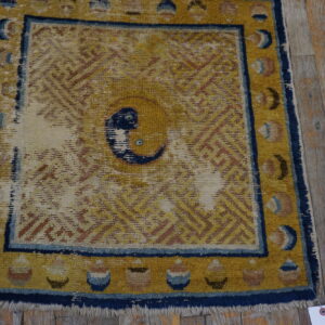 Worn golden yellow rug with a blue border and central knot motif placed on rustic wood planks.
