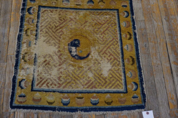 Worn golden yellow rug with a blue border and central knot motif placed on rustic wood planks.