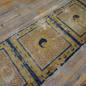 Distressed gold and blue runner with central dark motifs and geometric patterns rests on weathered wood floors.