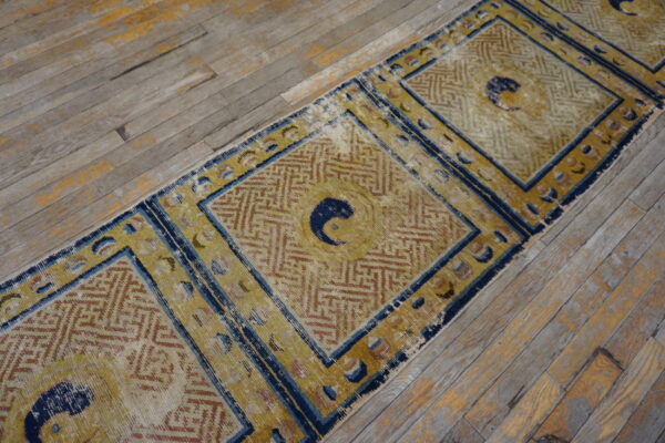 Distressed gold and blue runner with central dark motifs and geometric patterns rests on weathered wood floors.