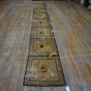 Yellow and blue runner rug with repeated panels displayed on rustic wood plank flooring.
