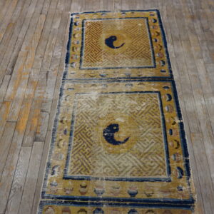 Worn runner rug featuring geometric gold and blue panels with central bird motifs on distressed grey wood floor.
