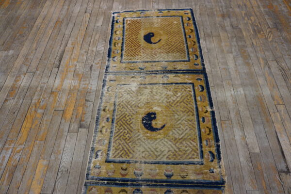 Worn runner rug featuring geometric gold and blue panels with central bird motifs on distressed grey wood floor.