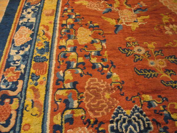 Close view of a high pile orange rug featuring navy and yellow floral designs and multi-banded striped borders.