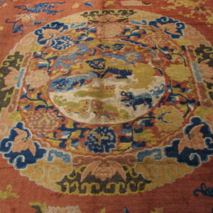 Textured red rug featuring a complex central design in blues, golds, and peach tones.