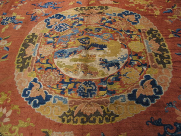 Textured red rug featuring a complex central design in blues, golds, and peach tones.