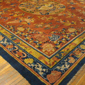 Rust-colored rug with complex blue, yellow, and salmon floral motifs and multi-banded borders lying on light wood flooring.