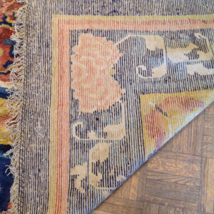 Low-pile rug border with navy stripes and pink flowers is folded over light brown parquet flooring.