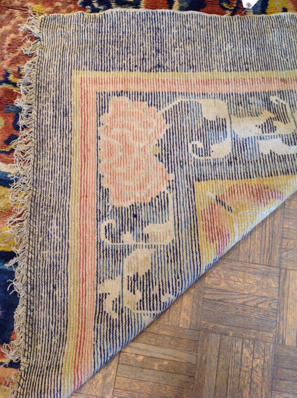 Low-pile rug border with navy stripes and pink flowers is folded over light brown parquet flooring.