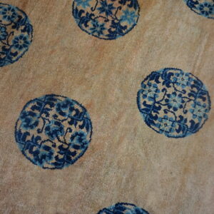 Close-up of a sandy-beige rug featuring repeating circular floral medallions in dark and light blue.