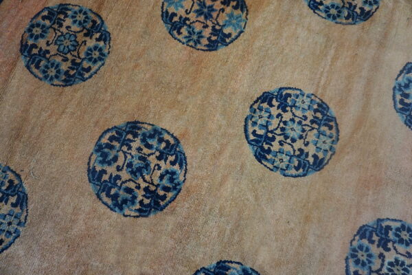 Close-up of a sandy-beige rug featuring repeating circular floral medallions in dark and light blue.