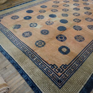 Large peach rug with repeating blue roundels and intricate blue border patterns, laid on wood flooring.