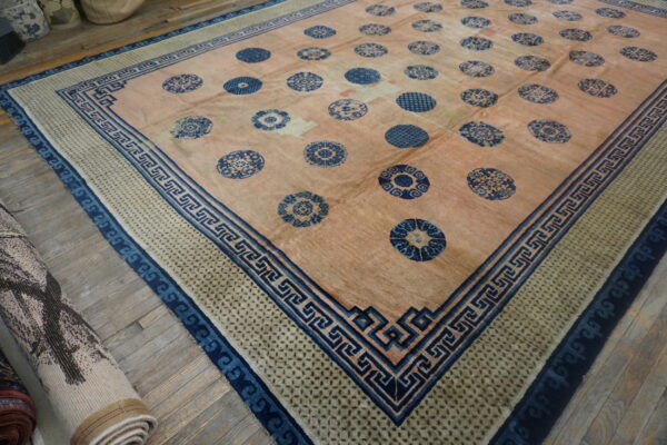 Large peach rug with repeating blue roundels and intricate blue border patterns, laid on wood flooring.