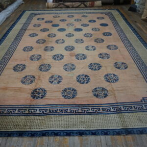 Large distressed rug with a pink field and scattered blue medallions displayed on wood flooring.