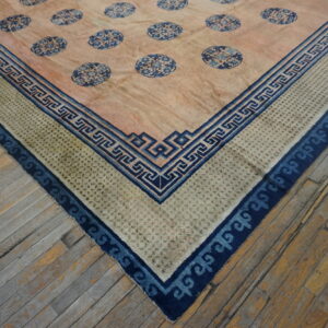 Corner view of a rug featuring a pink field, blue medallions, and intricate Greek key borders on wood floor.