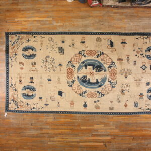 Tan rug with dark blue and rust stylized patterns, including a large central medallion, lying on wooden floorboards.