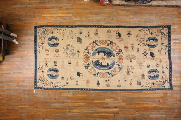 Tan rug with dark blue and rust stylized patterns, including a large central medallion, lying on wooden floorboards.