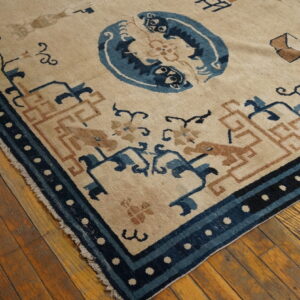 Beige rug featuring blue and rust patterns, including a central medallion and geometric border, resting on wood planks.