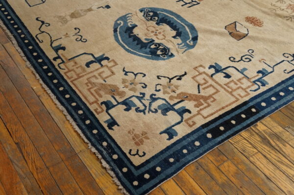 Beige rug featuring blue and rust patterns, including a central medallion and geometric border, resting on wood planks.