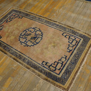 Peach and gold rug with a dark blue geometric fretwork pattern rests on weathered wooden planks.