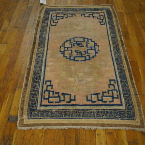 Small low-pile rug with a pale pink field and dark blue geometric pattern rests on distressed wood planks.