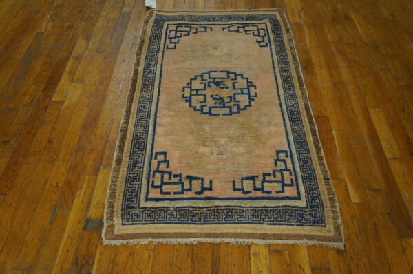 Small low-pile rug with a pale pink field and dark blue geometric pattern rests on distressed wood planks.
