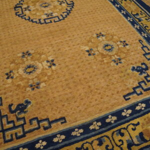 Tan and navy blue rug featuring floral medallions and geometric key pattern borders over hardwood flooring.