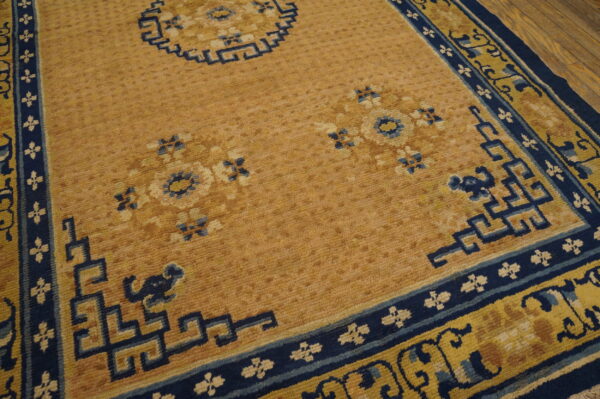 Tan and navy blue rug featuring floral medallions and geometric key pattern borders over hardwood flooring.