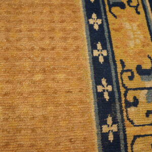Textured gold rug pile with a dark blue and yellow ornamental border rests on light wooden flooring.