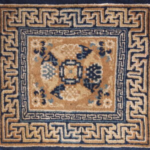 Tan and navy square rug with a stylized floral center and complex Greek key borders.