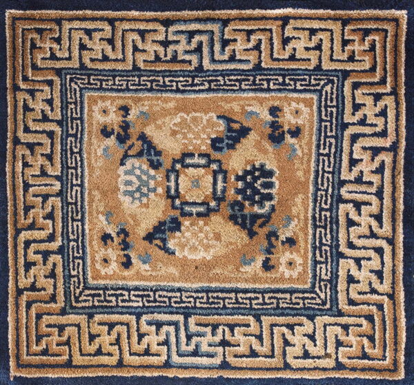 Tan and navy square rug with a stylized floral center and complex greek key borders.